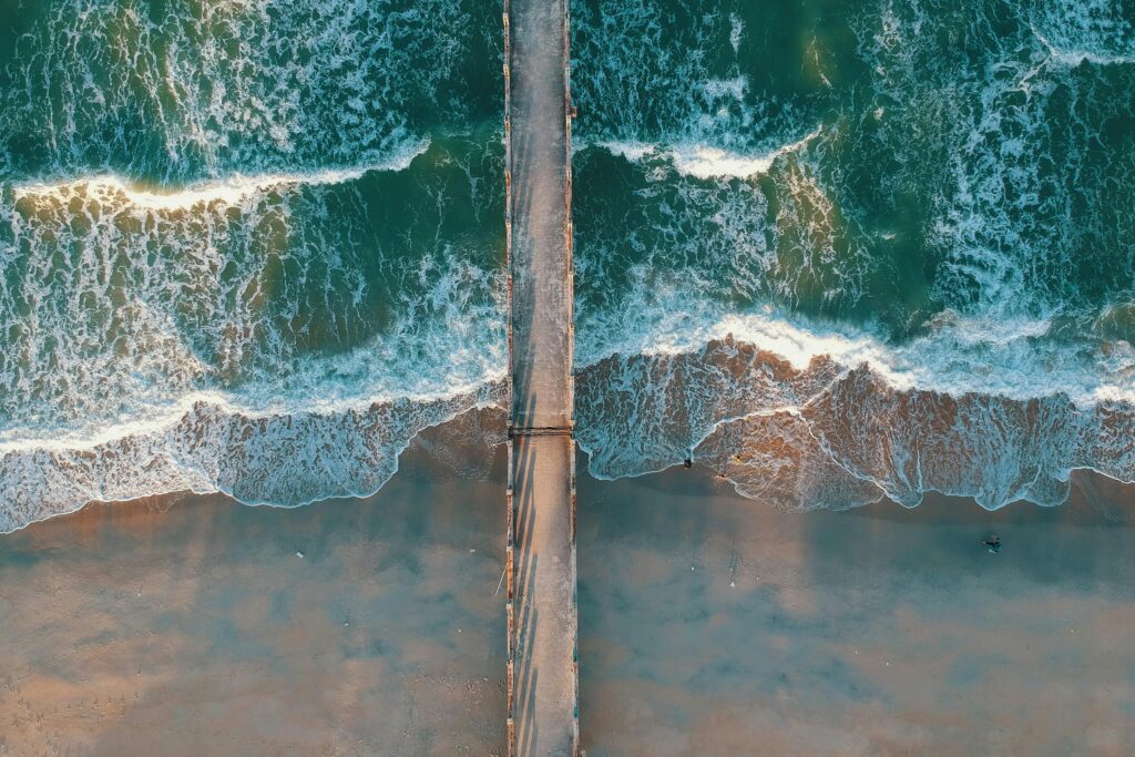 Drone shot of Kijal beach with waves crashing against the pier in Terengganu, Malaysia.