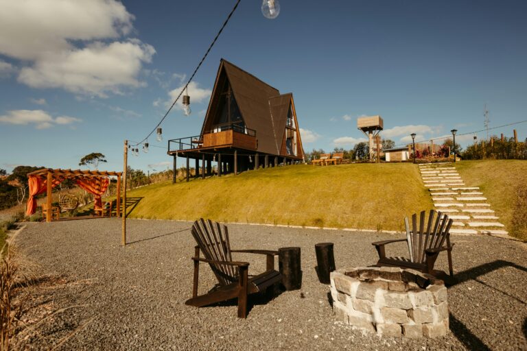 A rustic A-frame cabin with a firepit and chairs, ideal for relaxation in a serene rural landscape.