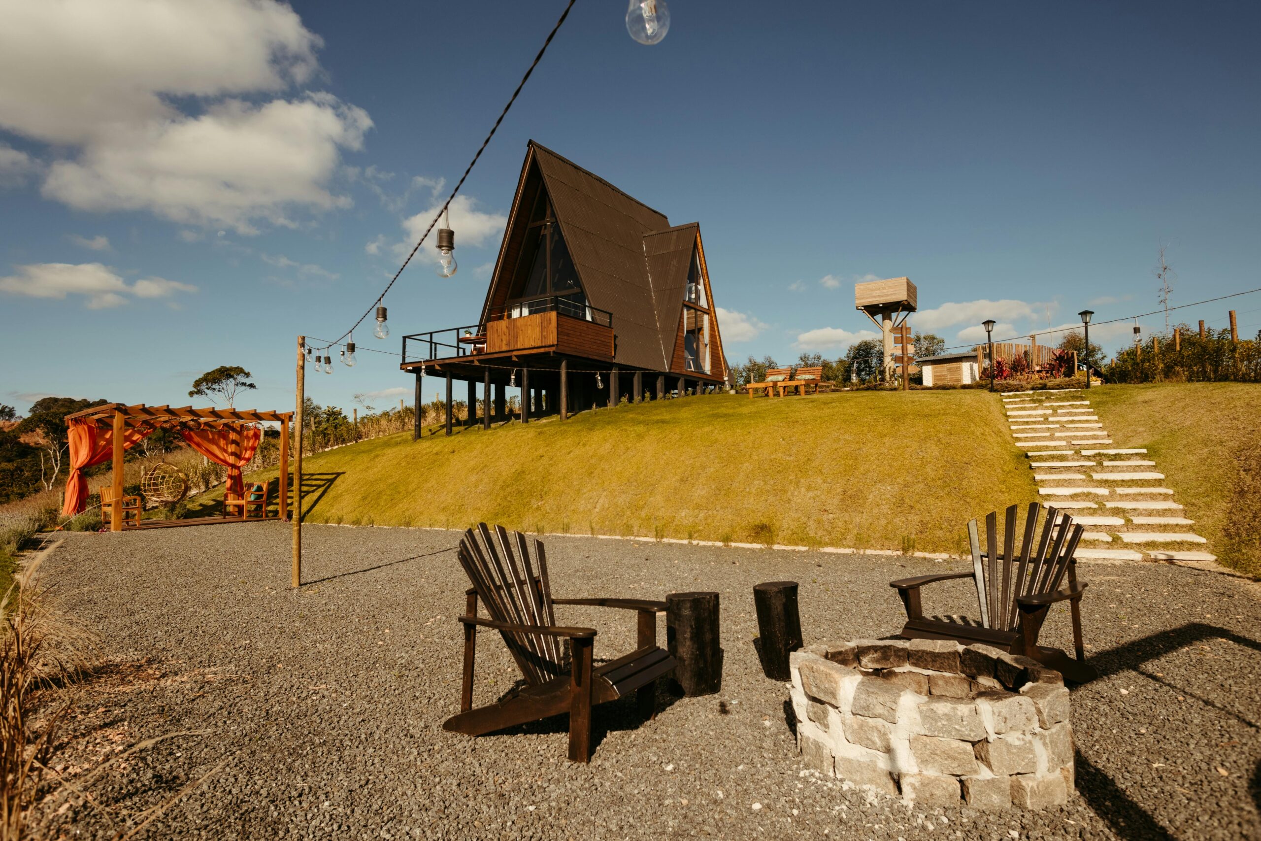 A rustic A-frame cabin with a firepit and chairs, ideal for relaxation in a serene rural landscape.
