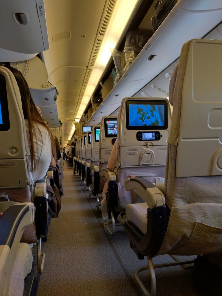 View of an airplane cabin interior with passengers seated, featuring screens on seatbacks.
