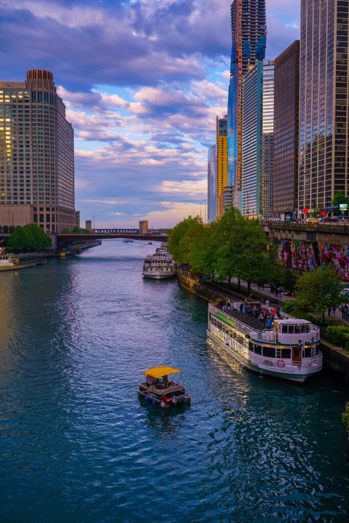 Elegant view of the Chicago River lined with modern skyscrapers and vibrant boats during sunset.