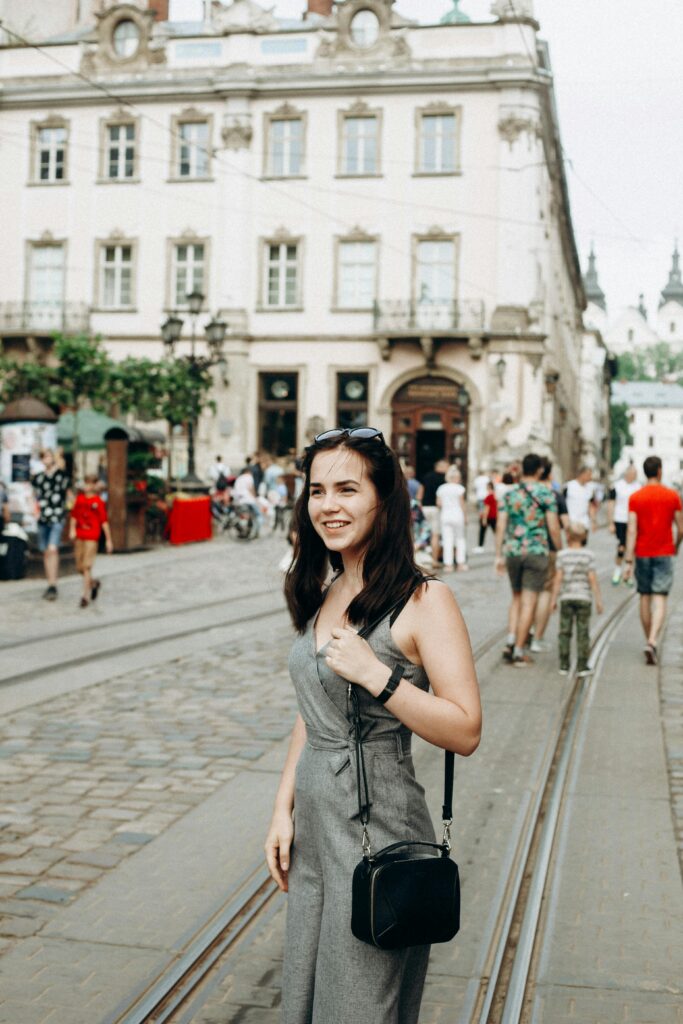 Young woman in stylish attire smiling on a bustling European city street. Perfect for travel and lifestyle themes.