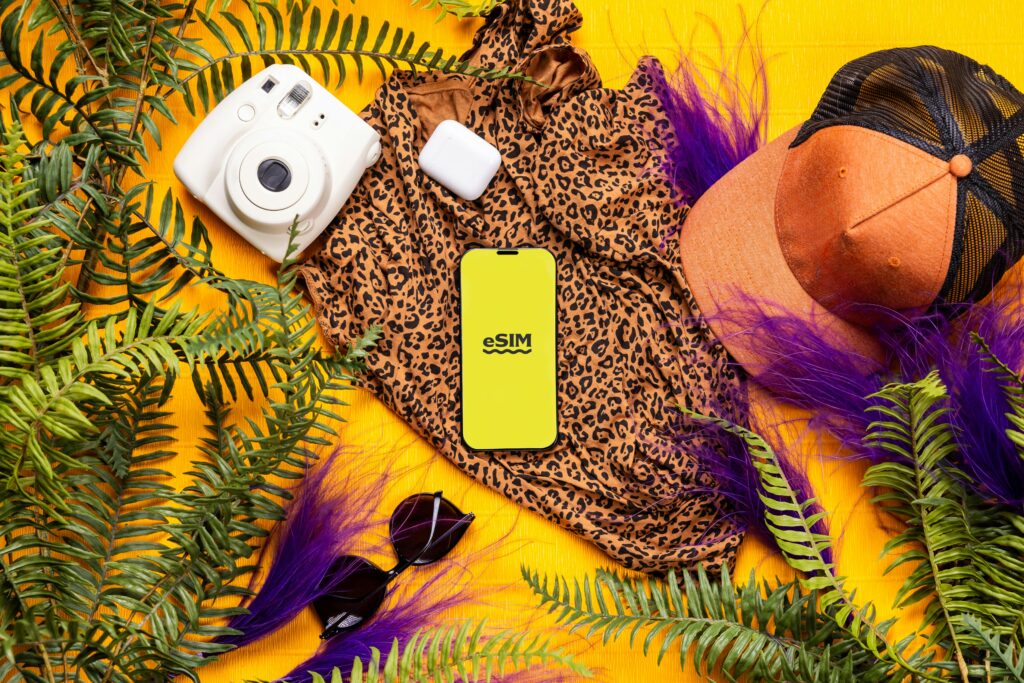 Flat lay of summer travel essentials featuring a leopard print dress, gadgets, and greenery on a bright yellow background.
