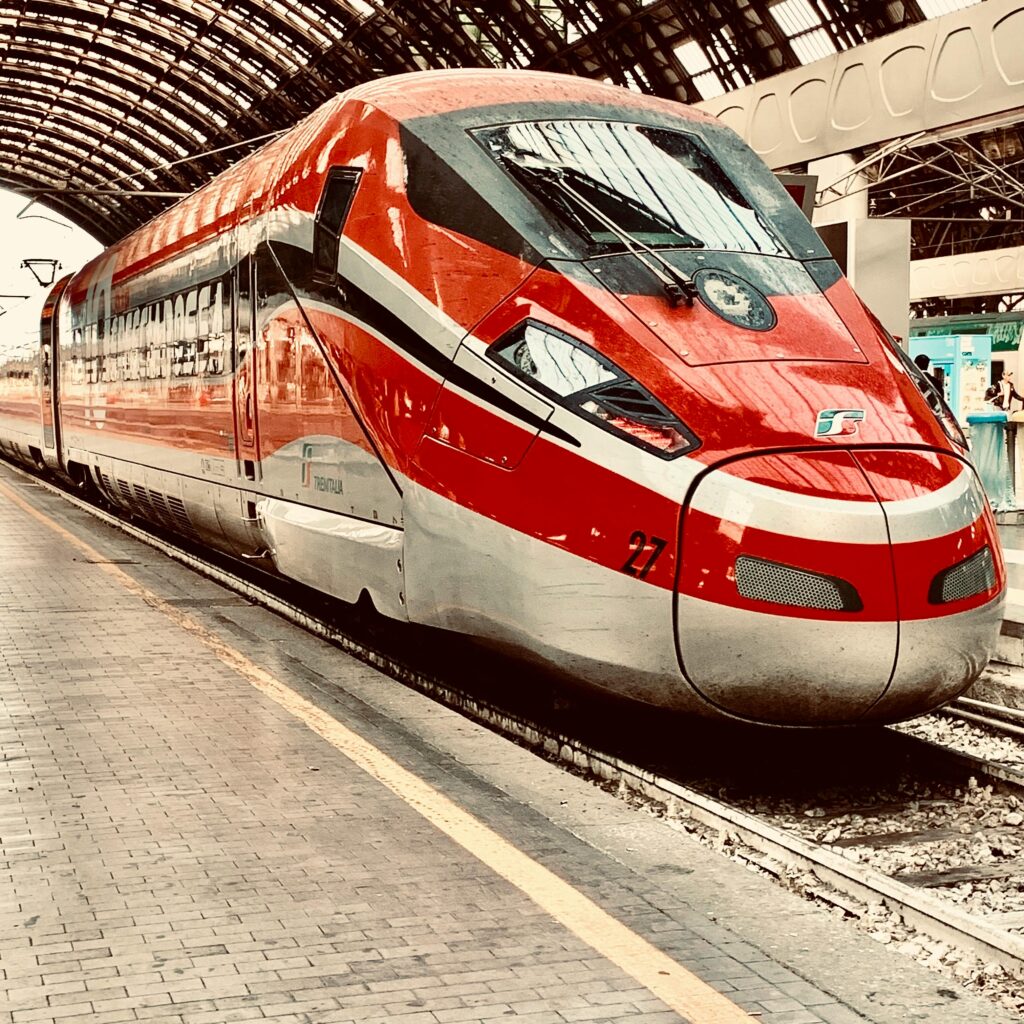 High-speed red train at Milan's iconic Centrale Station, showcasing Italian railway efficiency.