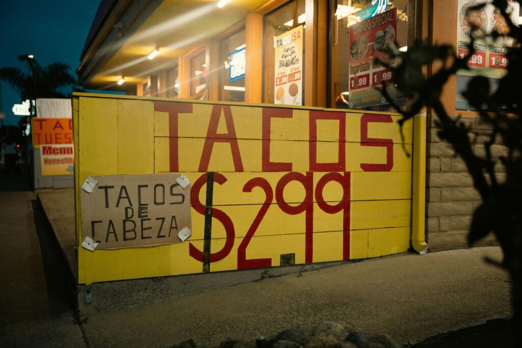 Street view of a taco stand with large yellow sign advertising tacos for $2.99, captured at night.