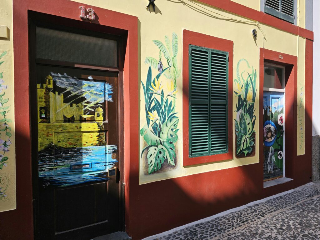 Colorful street art on Mediterranean-style building facade with red accents and shutters.