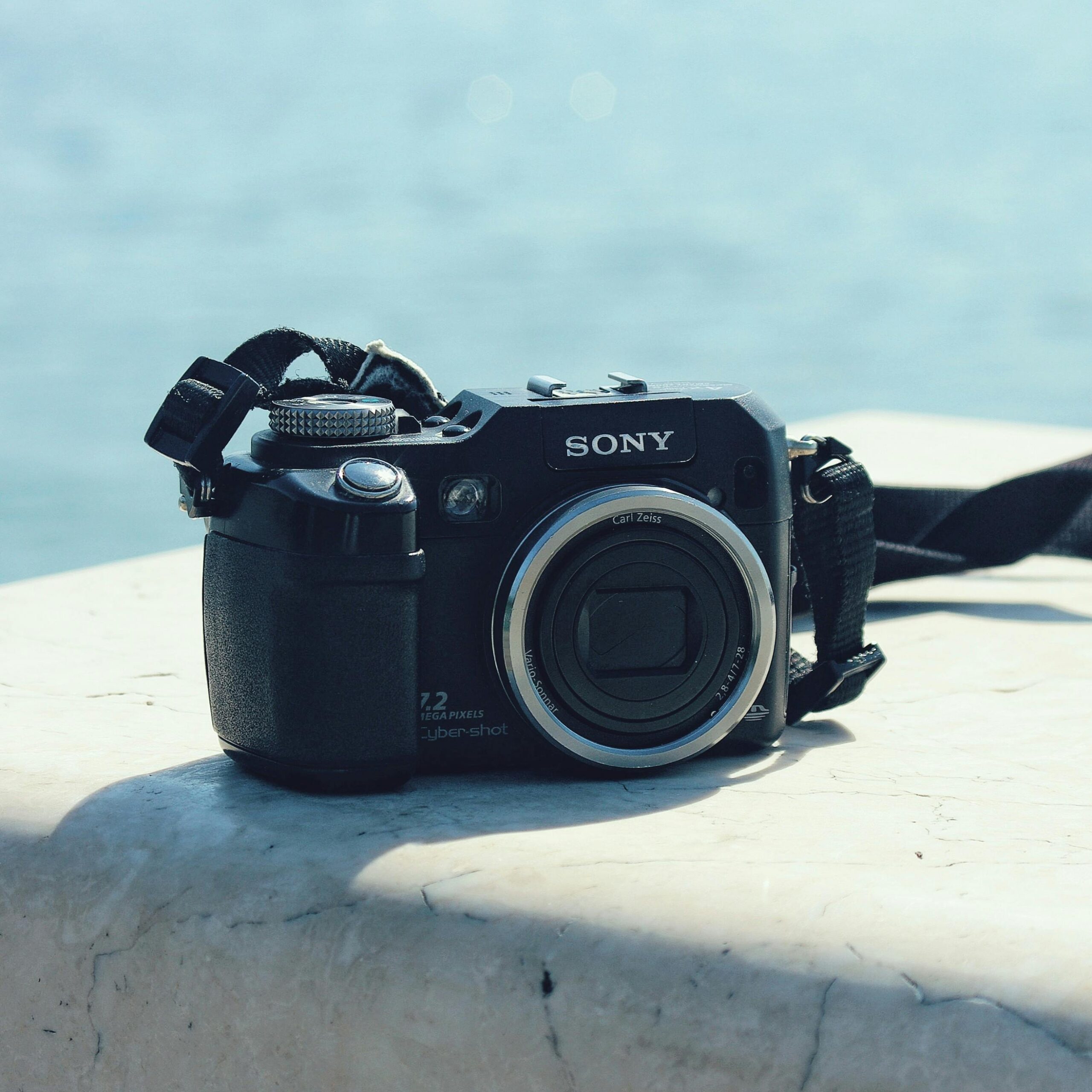 A classic Sony camera rests on a marble surface with a blurred blue ocean background.