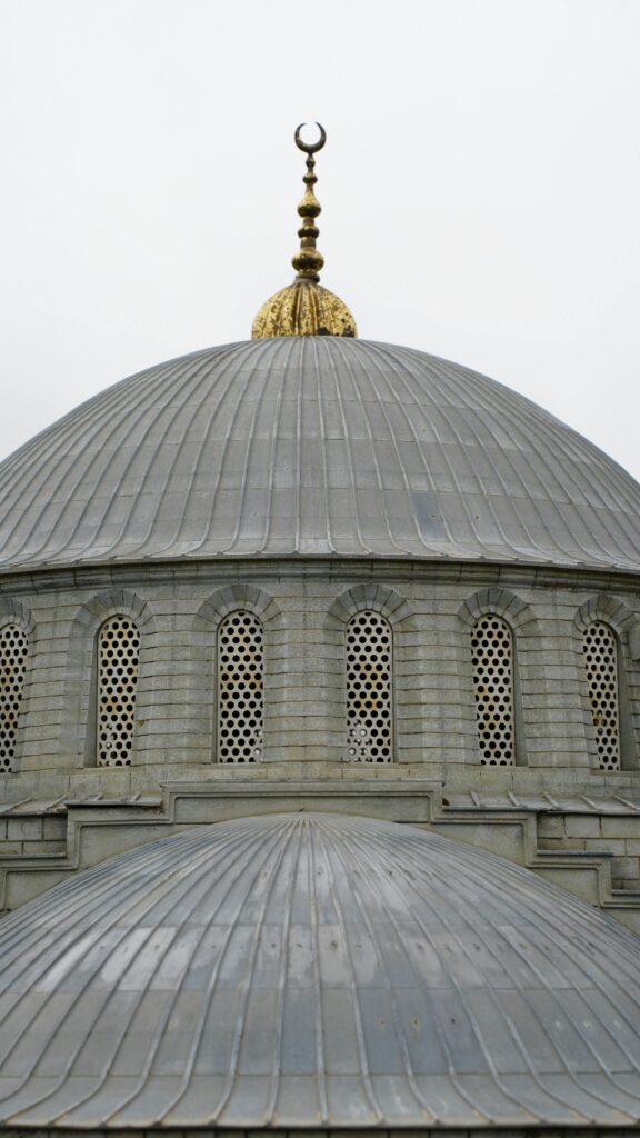 A close-up of a mosque dome featuring a crescent symbol against a cloudy sky.