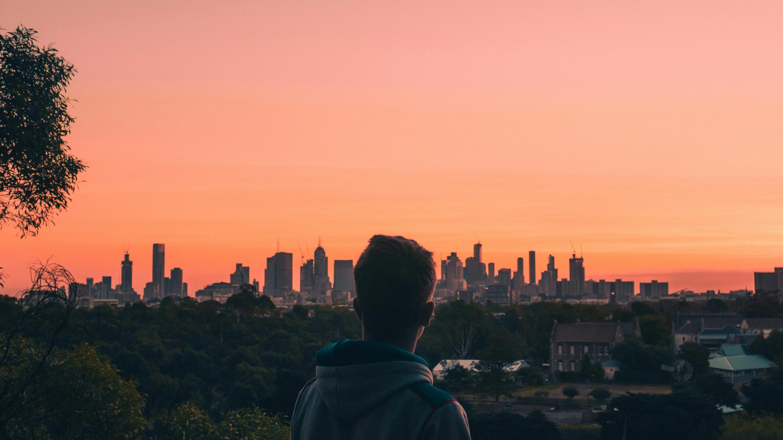 A person admires the Melbourne skyline at sunset, creating a stunning silhouette against a vibrant sky.