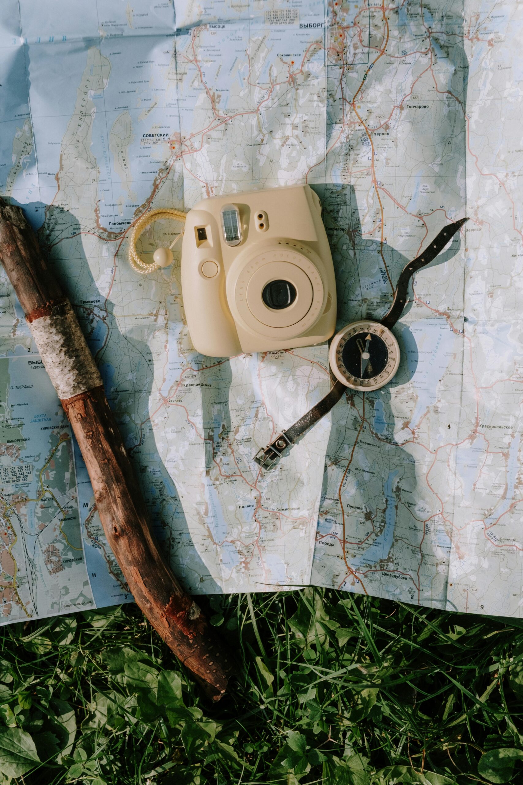 Flat lay of vintage camera, compass, and walking stick on a map outdoors. Perfect for travel and adventure themes.