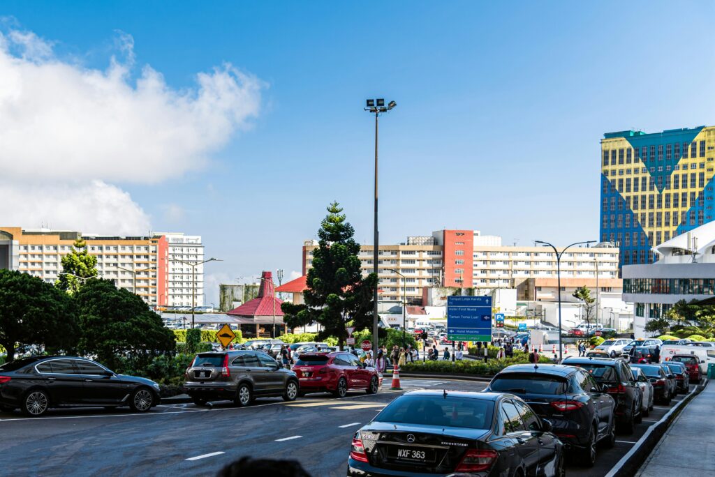 Urban scene in Genting Highlands with parked cars and city buildings under a bright sky.