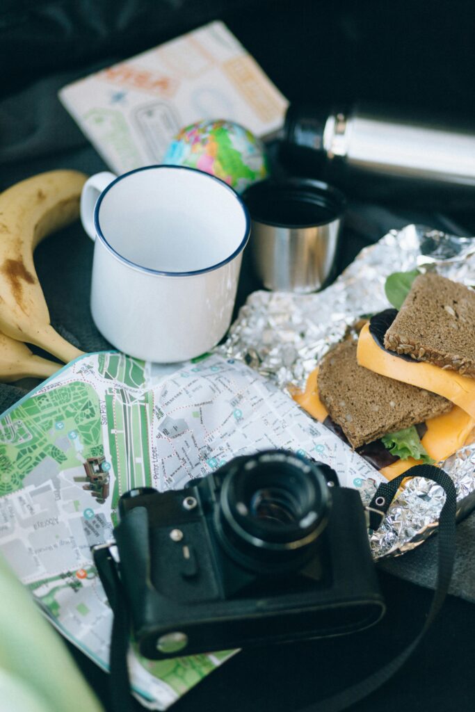 A flat lay of travel essentials including a map, camera, sandwich, and banana for a journey.