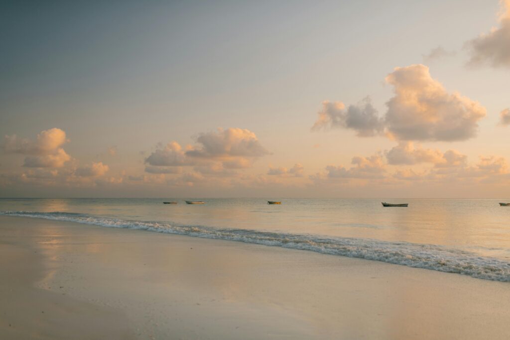Peaceful sunset with boats and gentle waves on a tropical beach, ideal for relaxation concepts.