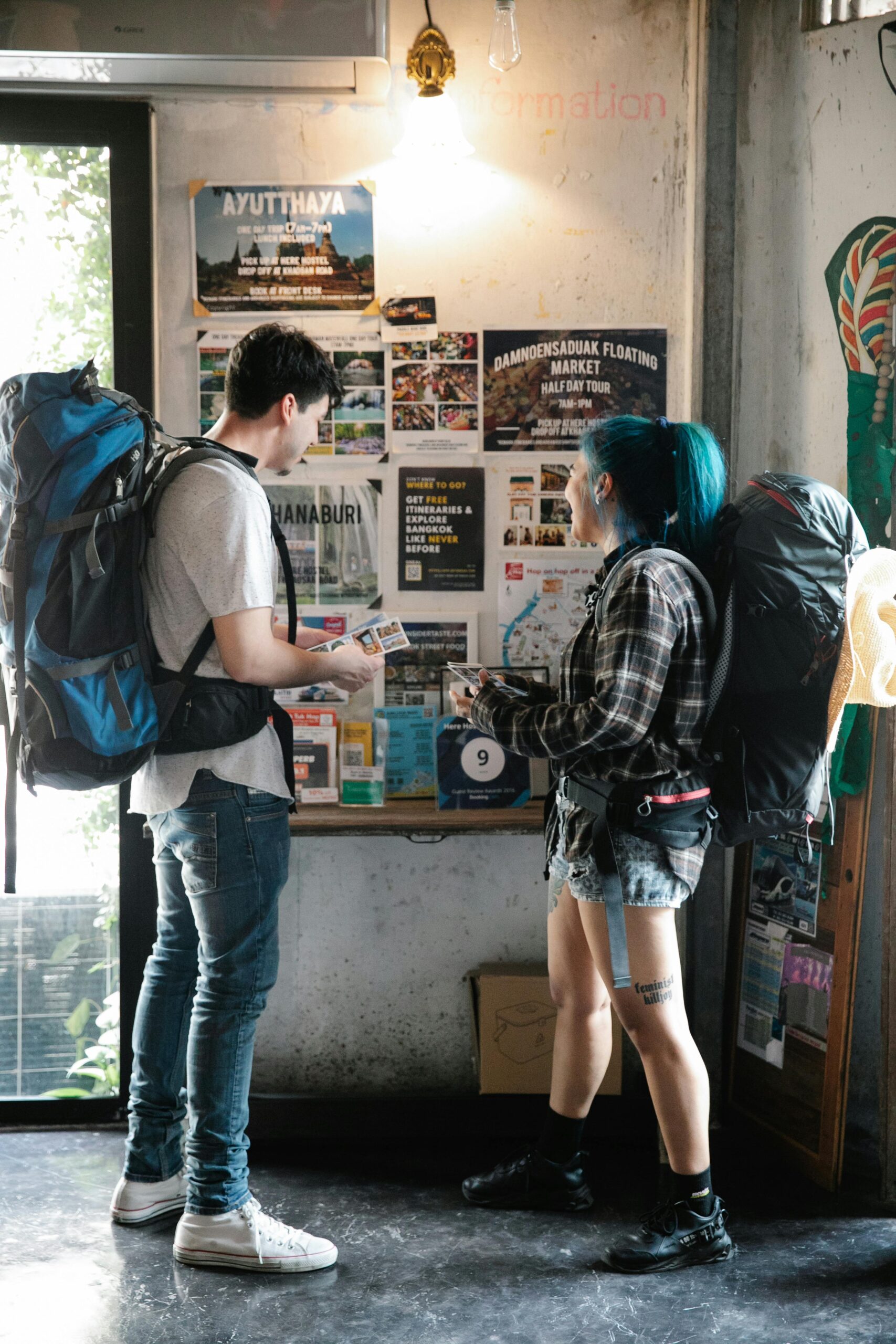 A young couple with backpacks examining travel brochures indoors, planning their next urban adventure.
